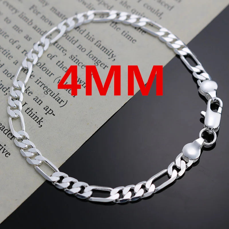 A silver charm necklace and bracelet set displayed on a piece of paper.