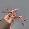A hand holds a pair of clear metal anti-blue light eyeglasses with rose gold accents against a gray background.