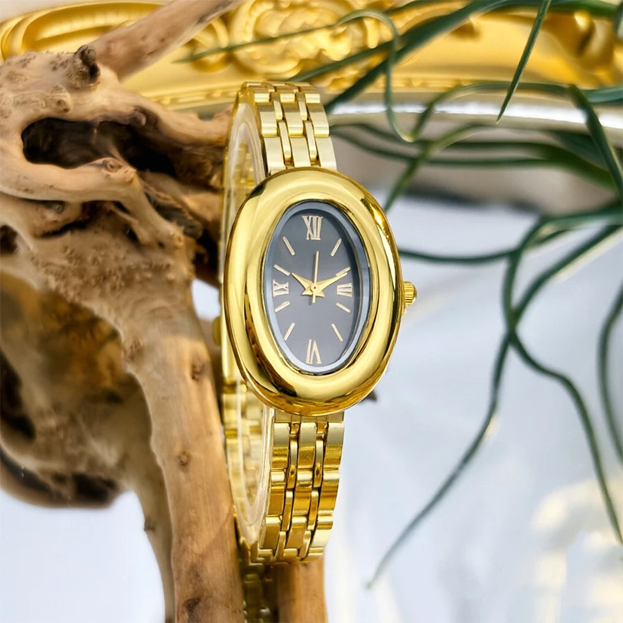 Reloj vintage dorado con esfera plateada y pulsera de oro, junto a una rama seca.