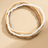 A set of multi-layered boho anklets featuring small beads in cream, white, and tan colors.