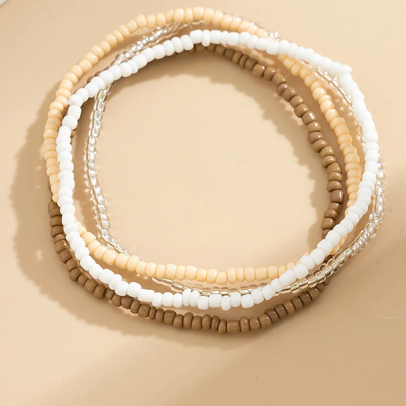 A set of multi-layered boho anklets featuring small beads in cream, white, and tan colors.