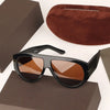 A pair of black oversized pilot sunglasses with brown lenses resting on a dark brown box.