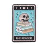 A tarot card enamel pin featuring a skull resting on a stack of books with celestial symbols.
