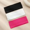 A pack of three solid color fashion headbands in black, white, and pink laid on a beige surface.