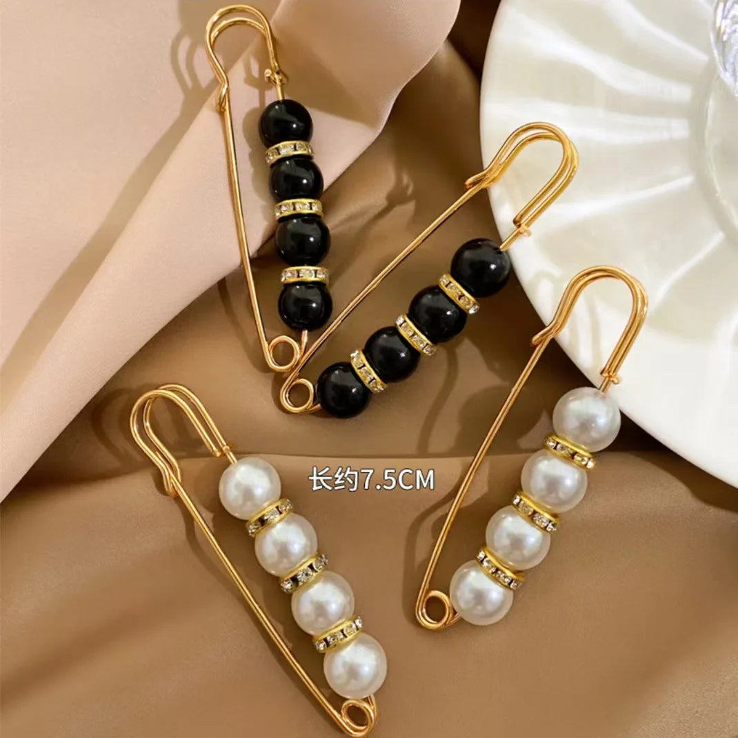 Gold-toned heavy duty pearl safety pins with black beads and white pearls displayed on a beige background.
