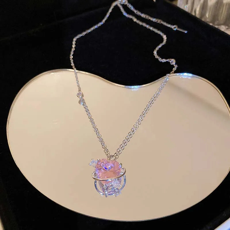 A delicate silver chain necklace featuring a pink heart-shaped zircon pendant displayed on a light background.