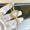 A hand wearing a white glove holds a gold-toned sparkling heart rhinestone quartz watch.