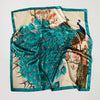 A luxurious teal satin silk scarf featuring a vibrant pattern of birds and floral elements on a cream background.