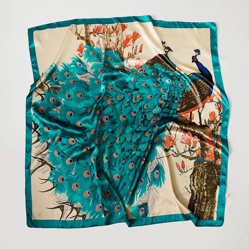 A luxurious teal satin silk scarf featuring a vibrant pattern of birds and floral elements on a cream background.