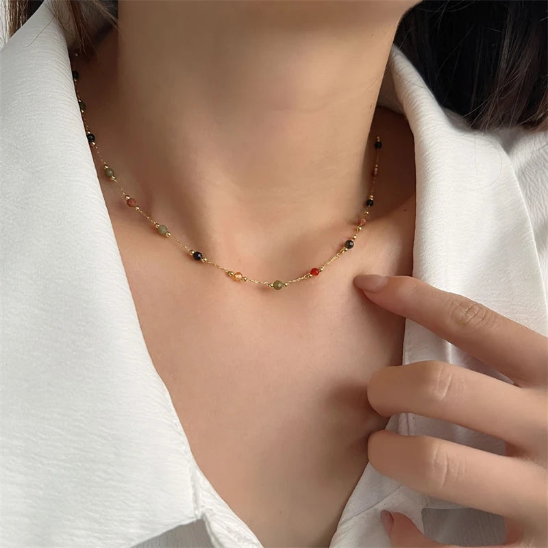 A delicate gold-toned beaded necklace with various colored beads is displayed against a white blazer.