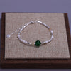 Sterling silver double heart charm bracelet with pearls and a green gemstone displayed on a brown wooden box.