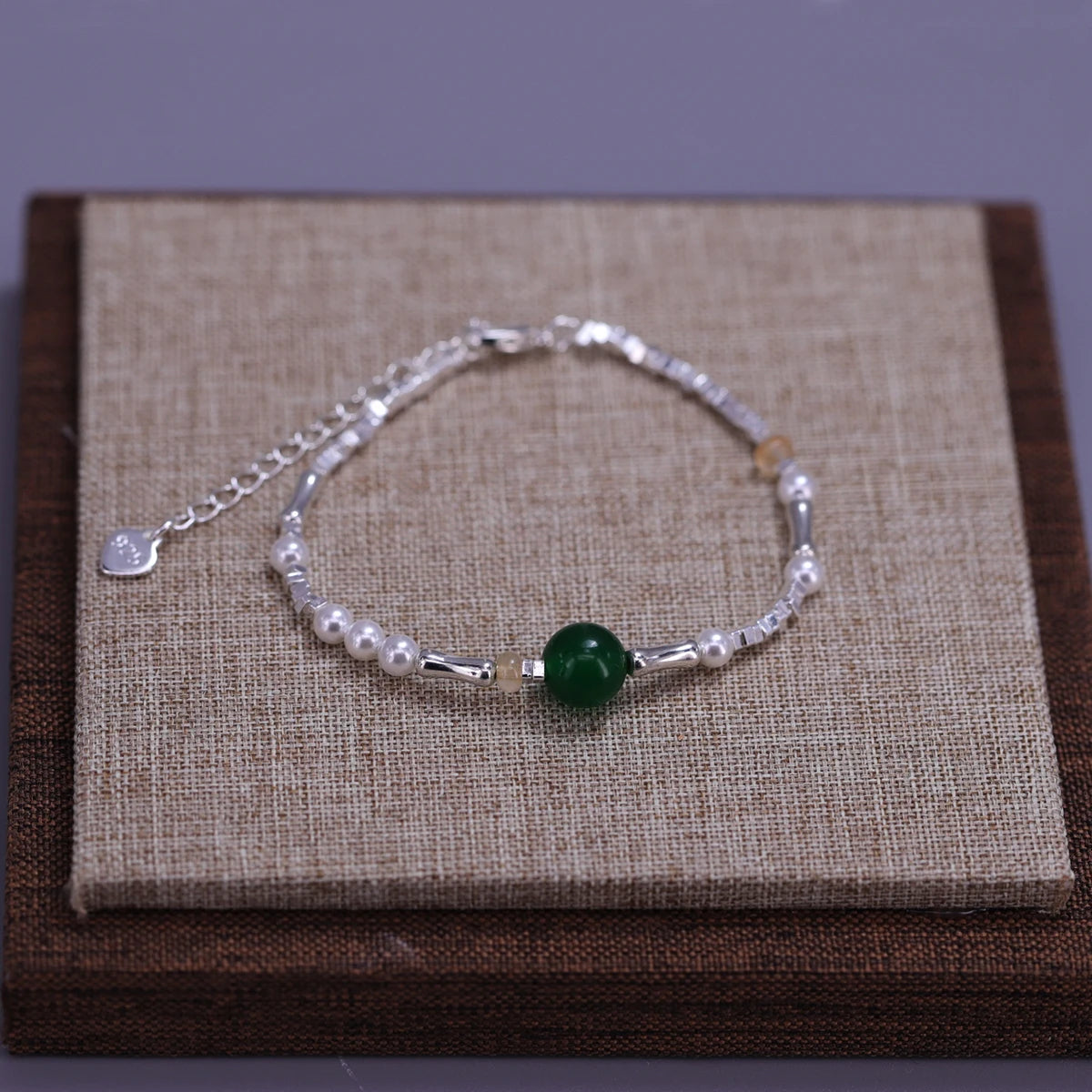 Sterling silver double heart charm bracelet with pearls and a green gemstone displayed on a brown wooden box.