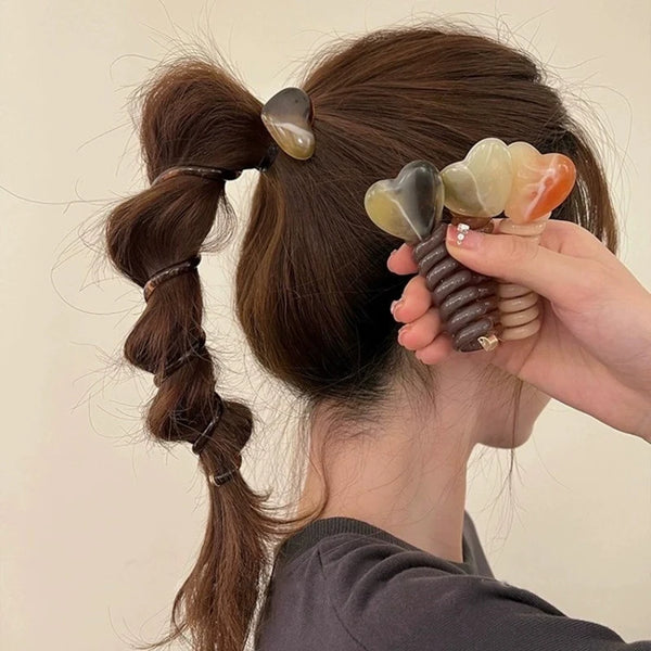 Una mano trenza cuentas de burbuja en forma de corazón en una trenza de pelo castaño para una diadema.