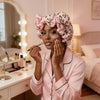 A woman applies a cosmetic product to her face while wearing a leopard print hair drying cap.