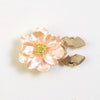 A delicate, pearlescent peach flower button cover with a gold glitter center and a brass-colored clasp.