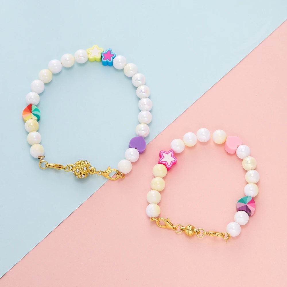 Weißes Perlenarmband mit farbigen Stern-Charms und goldenen Verschluss auf rosa-blauer Fläche.