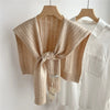 Chal de acrílico tejido beige colgado sobre una camisa blanca, expuesto en percha de madera.