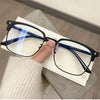 A pair of black anti-blue light clear framed eyeglasses resting on a white paper against a gray background.