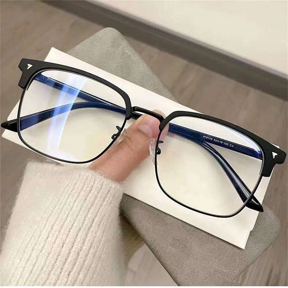 A pair of black anti-blue light clear framed eyeglasses resting on a white paper against a gray background.