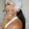 A woman wearing a sheer white lace trim veil and delicate gold jewelry, looking to the side.