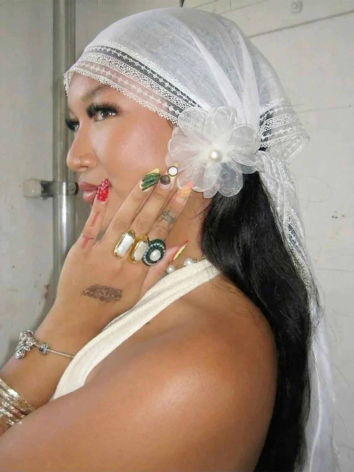 A woman wearing a sheer white lace trim veil and delicate gold jewelry, looking to the side.