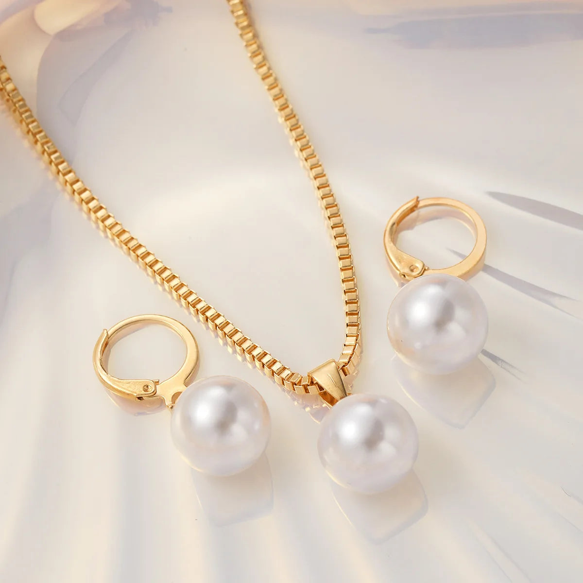A delicate gold chain necklace with pearl drops and a matching gold ring set displayed on a light surface.