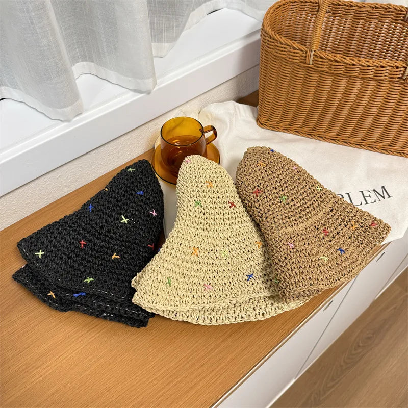 Tres sombreros de paja tejidos a mano en negro, beige y marrón sobre una superficie de madera.