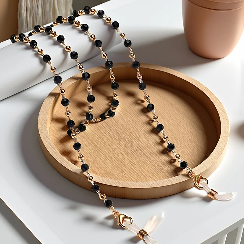 Gold and black crystal bead lanyards and chains displayed on a wooden tray.