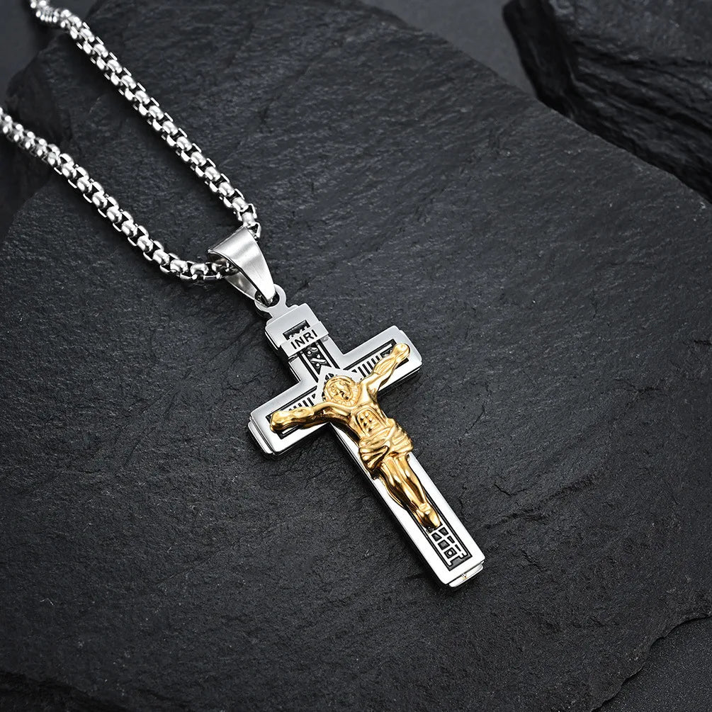 Colgante de cruz de Jesús chapado en oro con placa INRI grabada, colgando de una cadena de plata, sobre una piedra oscura.