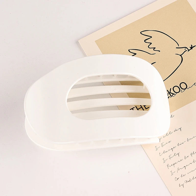 A white flat circular hair clip set is shown resting on a piece of light brown paper with a line drawing of a bird.
