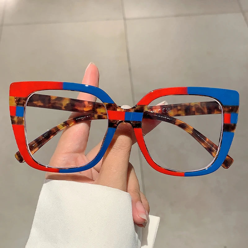 Eine Hand hält eine trendige, große, quadratische Brille mit mehrfarbigem Elfenbein- und blauen Akzenten.