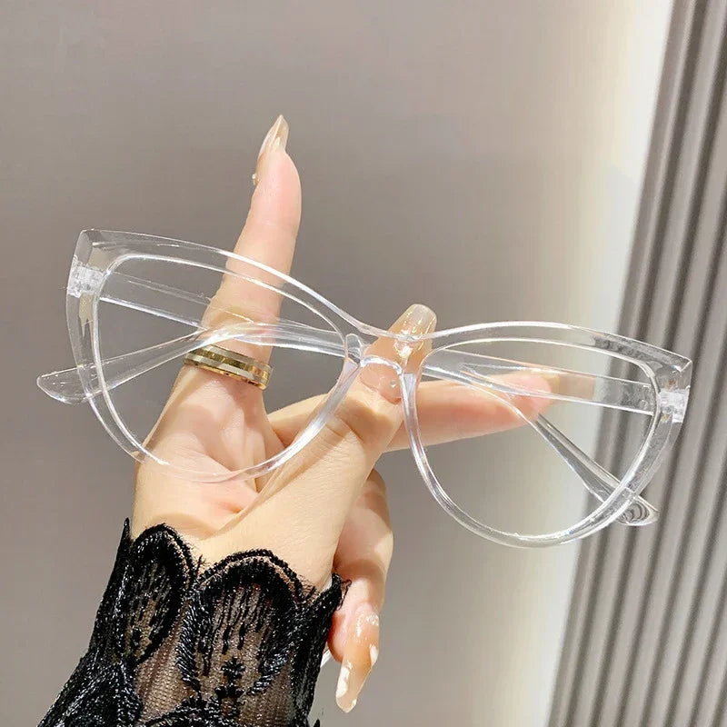 Eine Hand hält eine klare Vintage Cat-Eye-Lesebrille mit goldenen Akzenten vor einem hellen Hintergrund.