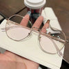 Une paire de lunettes fines à monture transparente avec une teinte rose pâle posée sur une surface blanche.