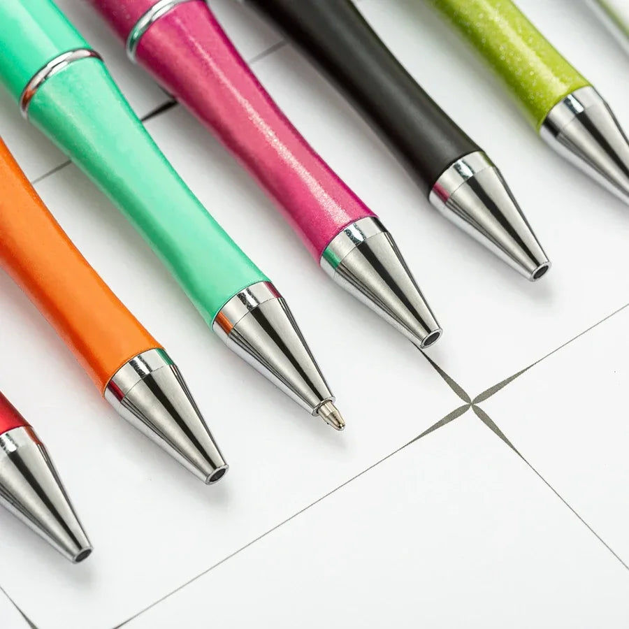 A collection of ten colorful beadable ballpoint pens arranged diagonally on a white surface.
