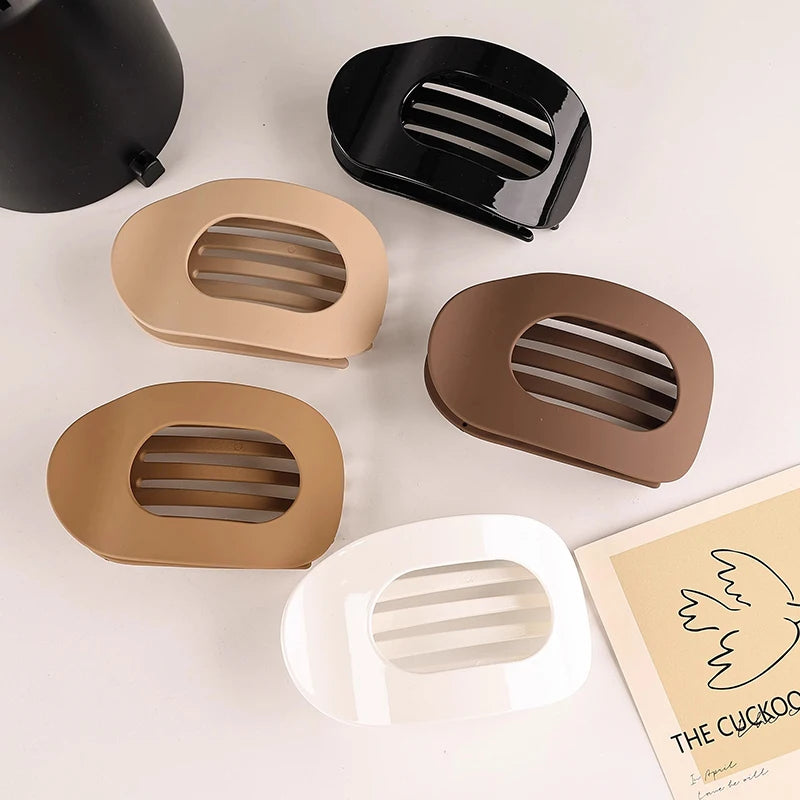 A set of five flat circular hair clips in various matte and glossy earth tones, including black, beige, and white.