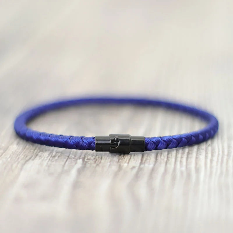 A close-up of a blue thread charm bracelet with a silver clasp resting on a light wooden surface.