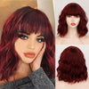 A woman models a long, curly red wine colored synthetic wig with bangs.