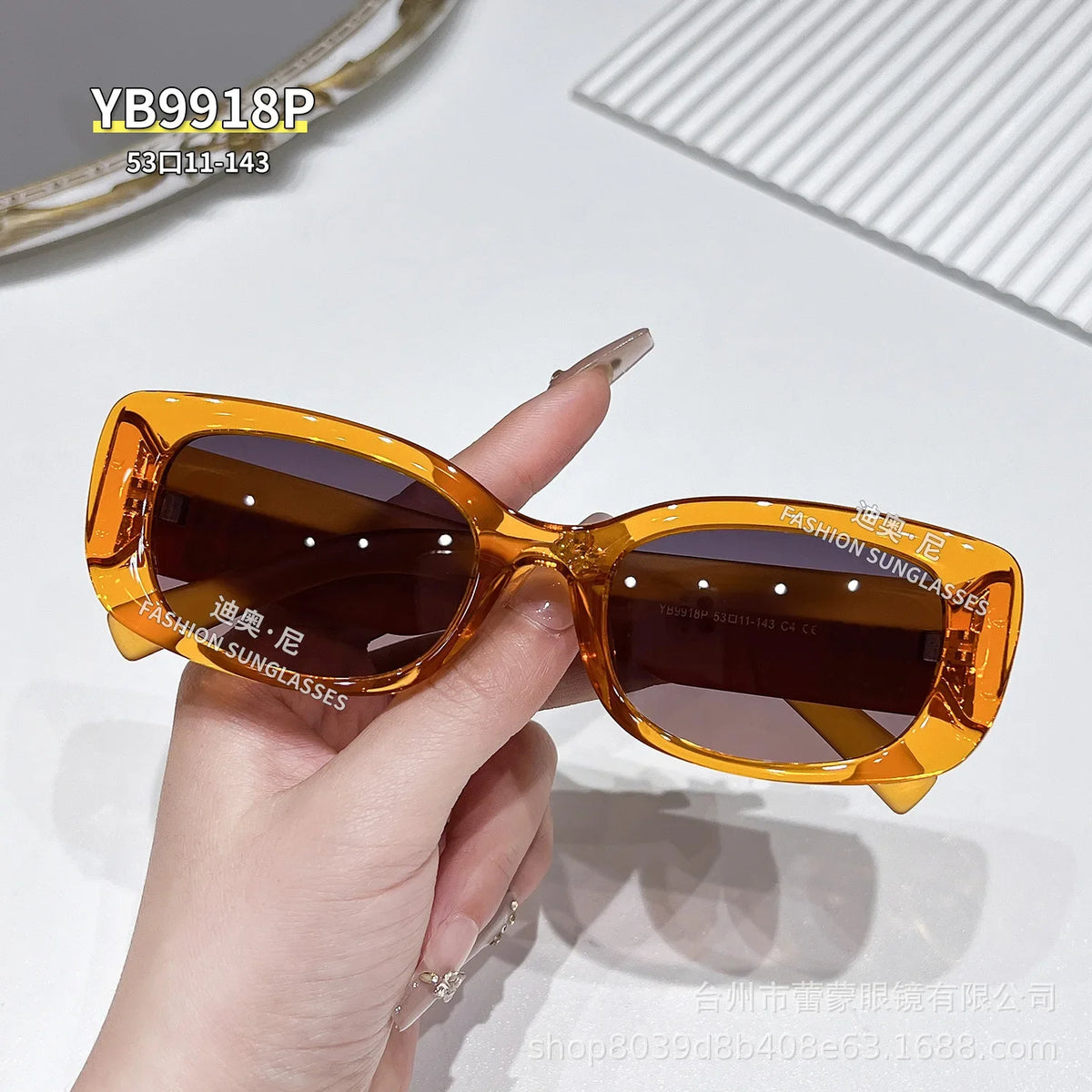 A hand holds a pair of amber-colored polarized fashion sunglasses against a white background.