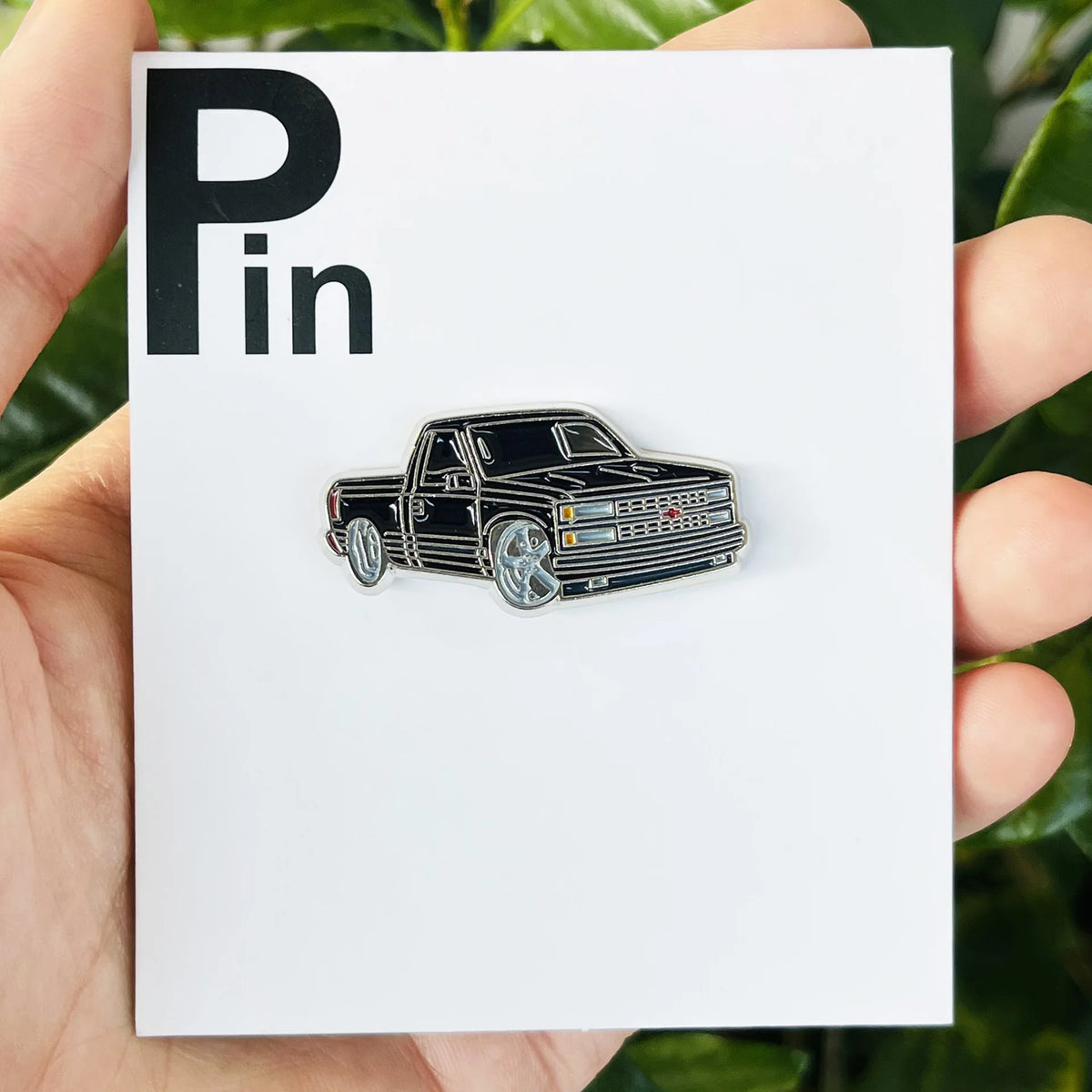 A silver metal clip pin featuring a black classic car with yellow and red accents.