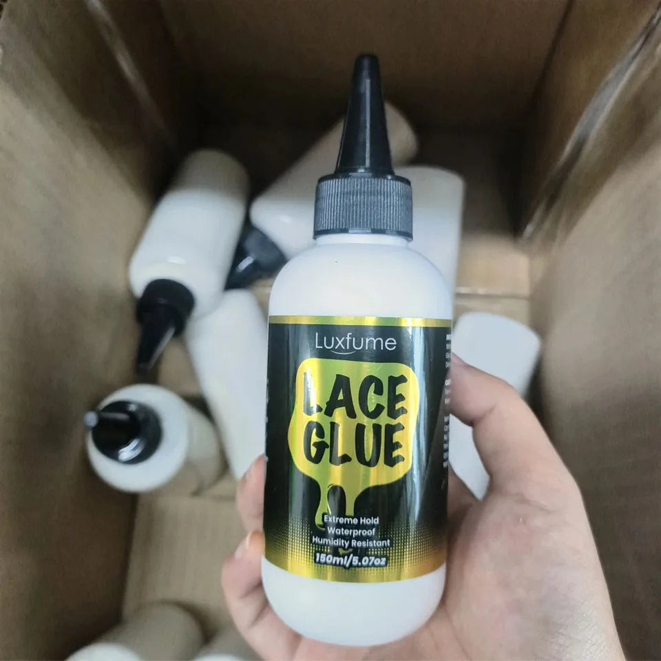 Eine Hand hält eine Flasche Luxfume Lace Glue, eine klare Flüssigkeit mit schwarzem und goldenem Etikett, in einer Kartonverp
