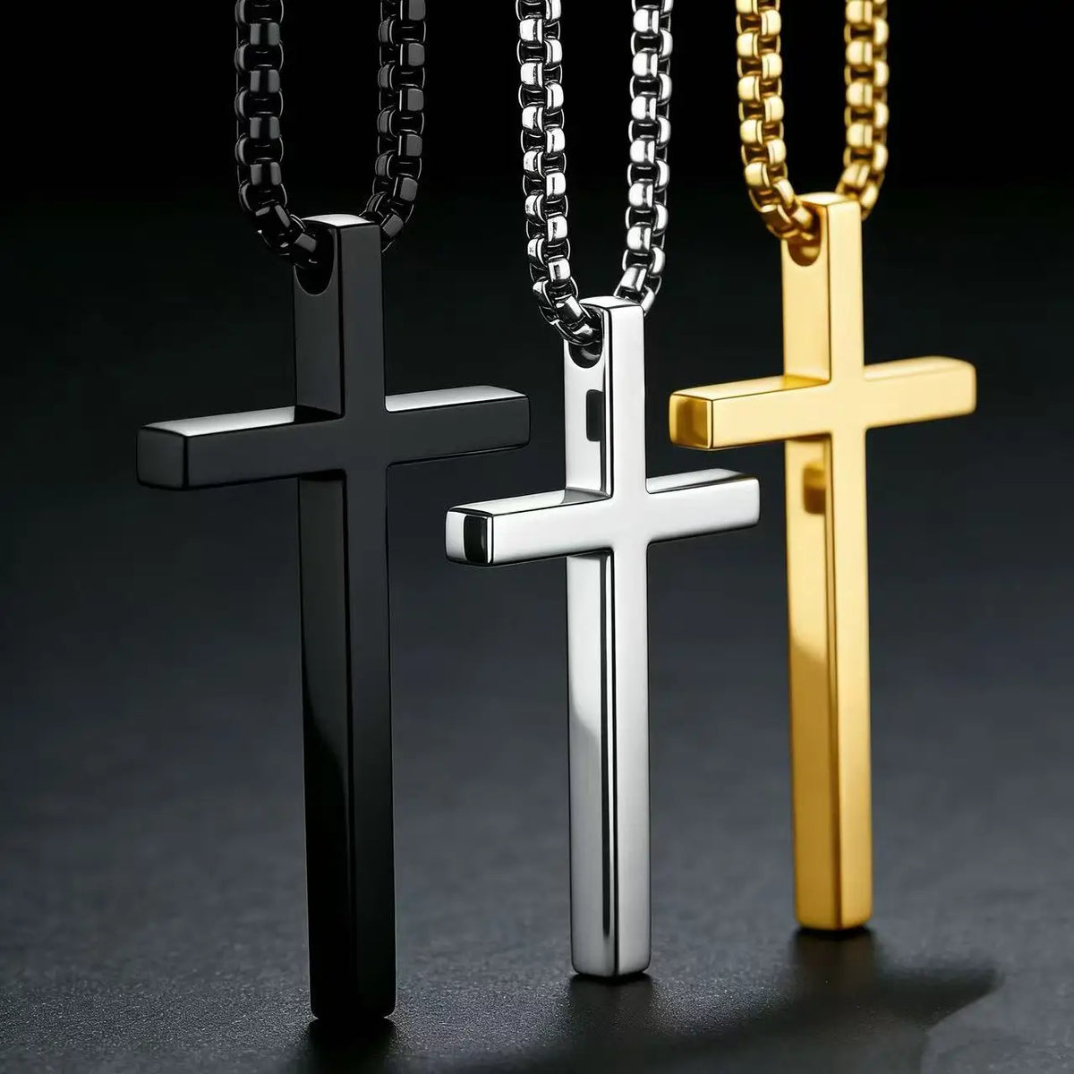 Three stainless steel cross pendant necklaces in black silver and gold displayed against a dark background