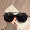 A pair of black double bridge oversized square sunglasses resting on a white surface.