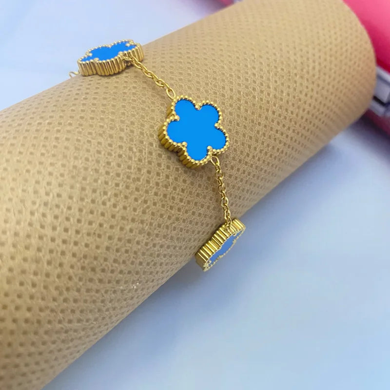 A gold plated stainless steel double-sided petal bracelet with blue floral charms is displayed on a beige cylindrical object.