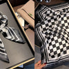 A black and white checkered silk scarf tied in a bow displayed in a box.