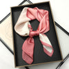 A pink and cream silk scarf tied in a bow displayed in a black picture frame.
