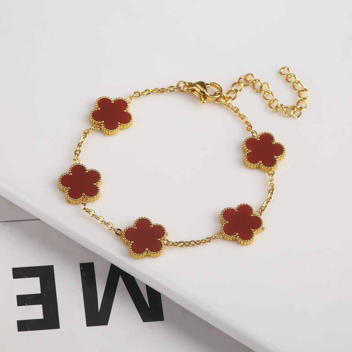 Pulsera de acero inoxidable chapada en oro con pequeños charms florales marrón rojizo.