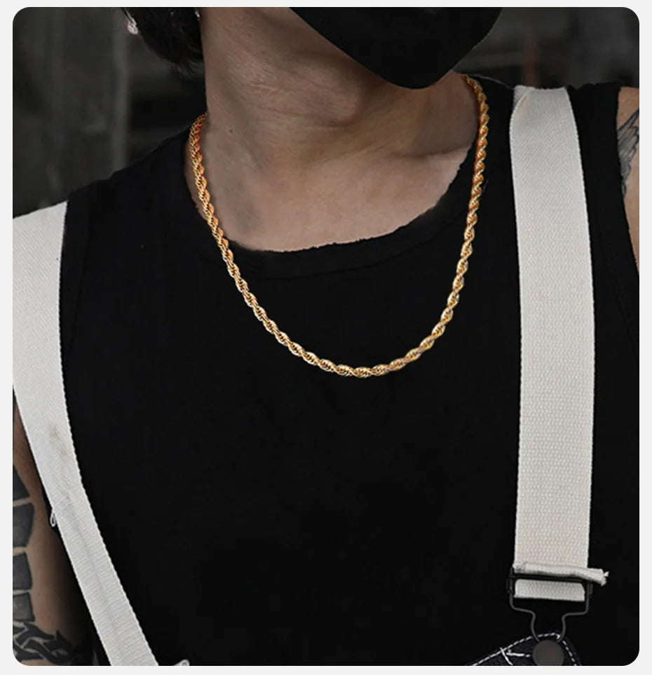 A close-up of a dainty gold rope chain necklace worn around the neck against a black shirt.