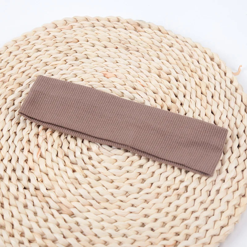 A brown knitted elastic headband lying on a light beige woven mat.