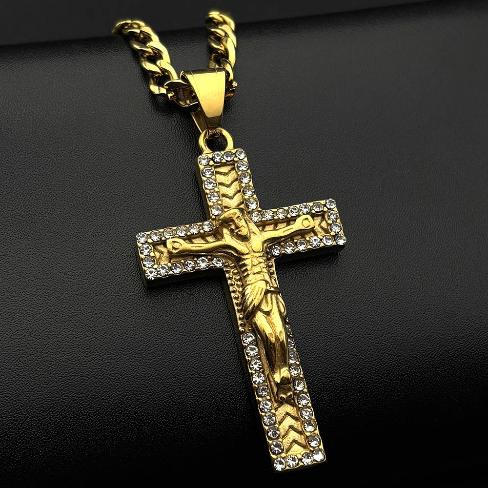 A gold-tone stainless steel cross pendant necklace with rhinestone accents displayed against a dark background.