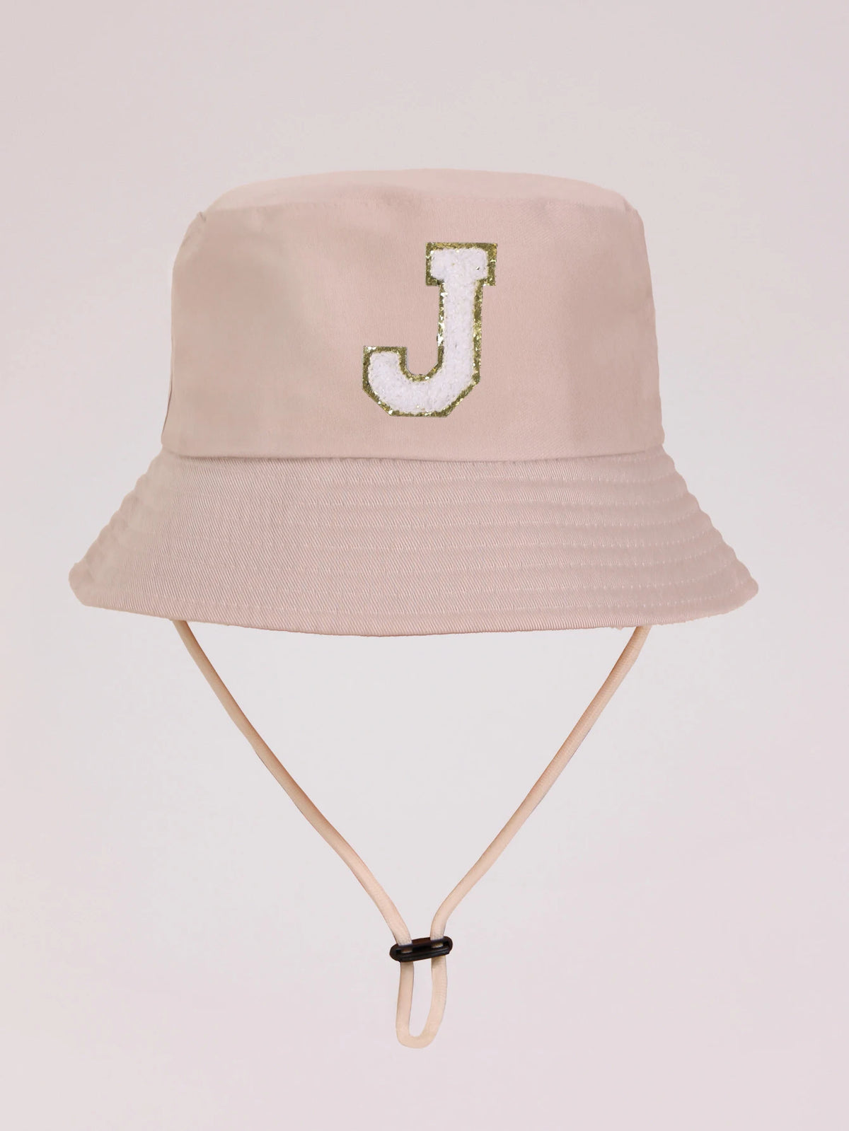 A light beige sun hat with a gold glitter letter J embroidered on the front.